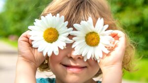Criança sorrindo segurando duas margaridas na frente dos olhos